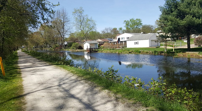 A gravel towpath runs parallel to the Ohio-Erie Canal with houses along its banks.